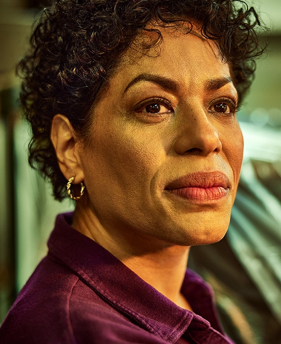Liza Colón-Zayas headshot wearing a burgundy collar shirt and gold earrings