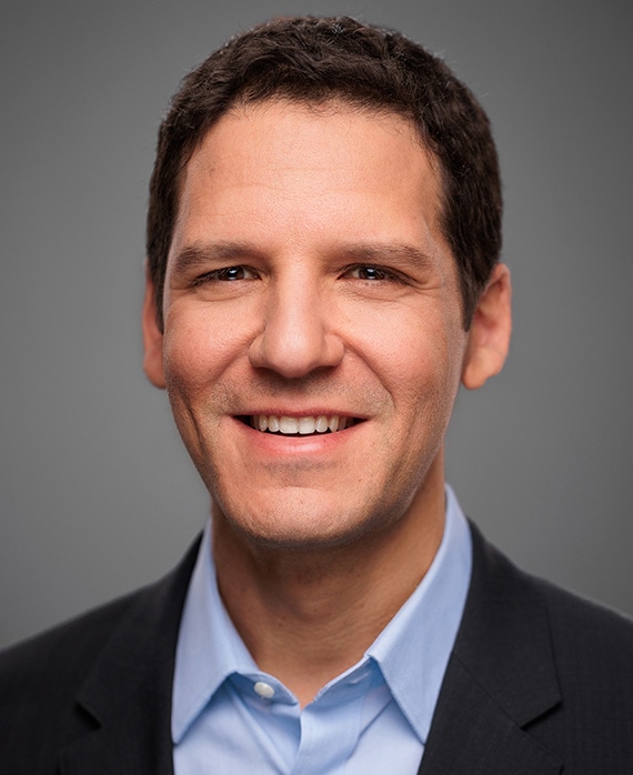 Ira Napoliello headshot in a blue button up and black suit.