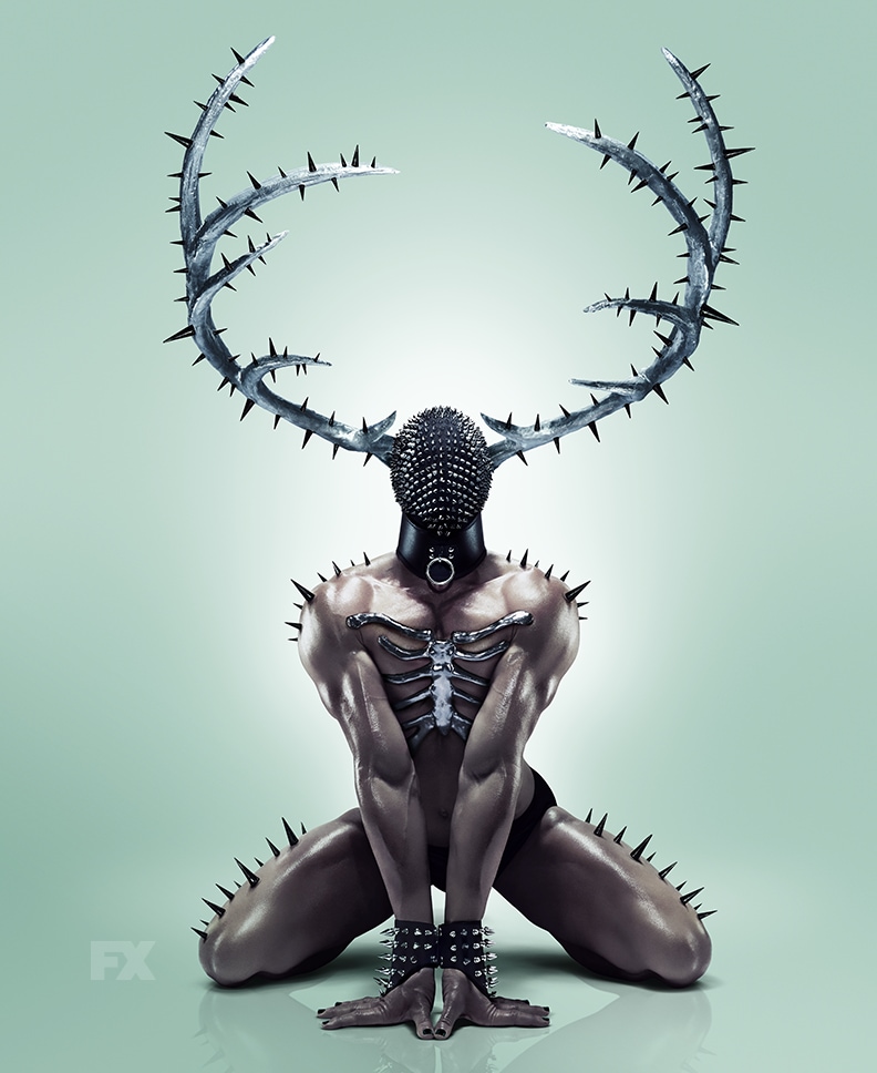 Muscular man on hands and knees wearing black mask, spiked antlers, and silver ribcage piece from FX'S AHS NYC