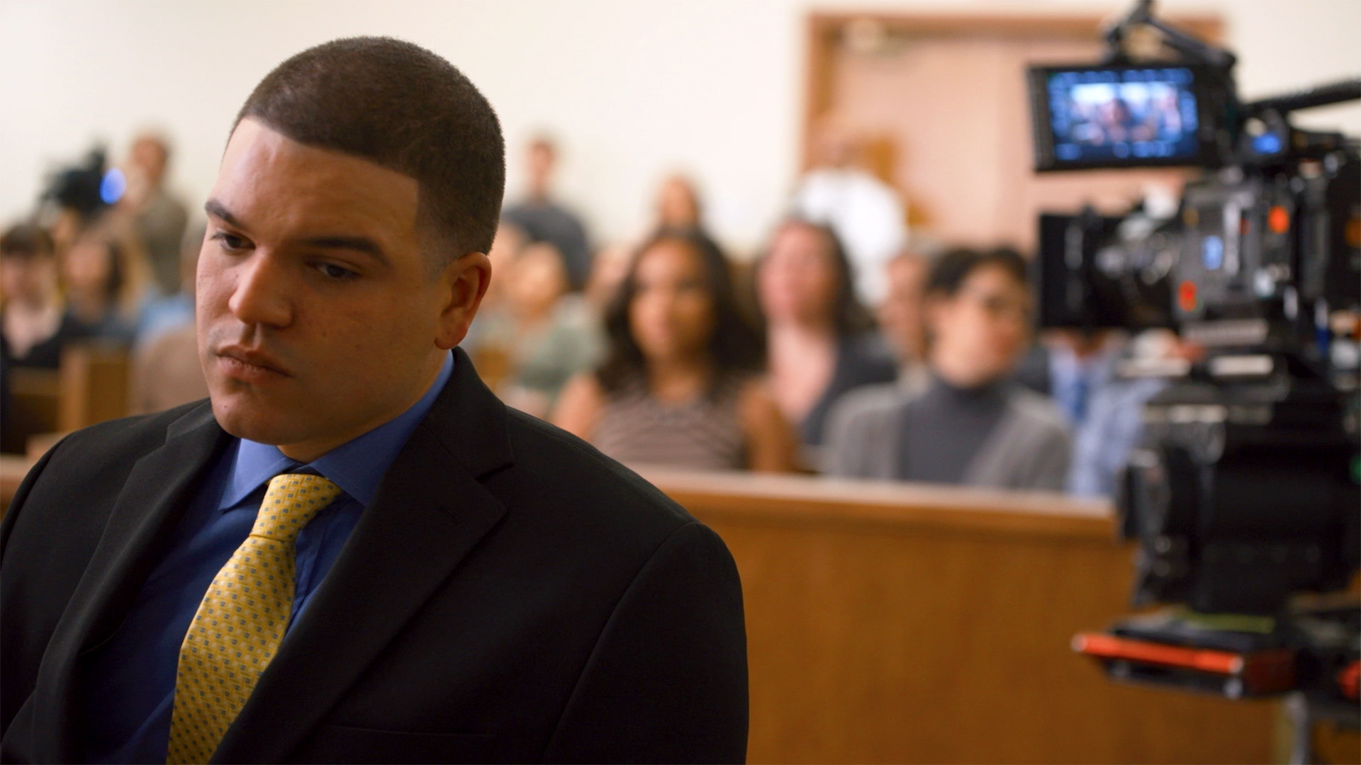 Aaron Hernandez sitting in a courtroom with a camera behind him.