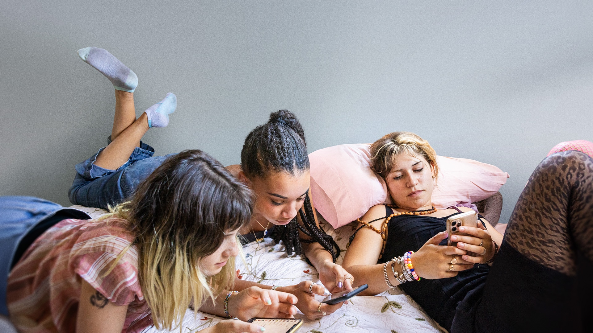 A group of three teenage girls look at their cell phones while lying on a bed.