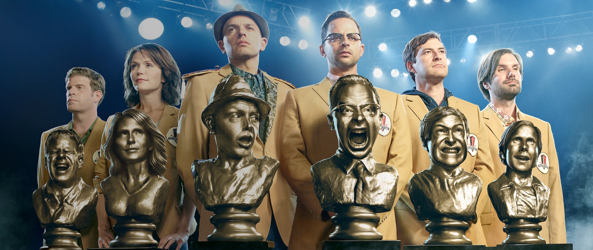 Group of friends lined on up a football field in Fantasy Football sports jackets standing behind golden busts of themselves