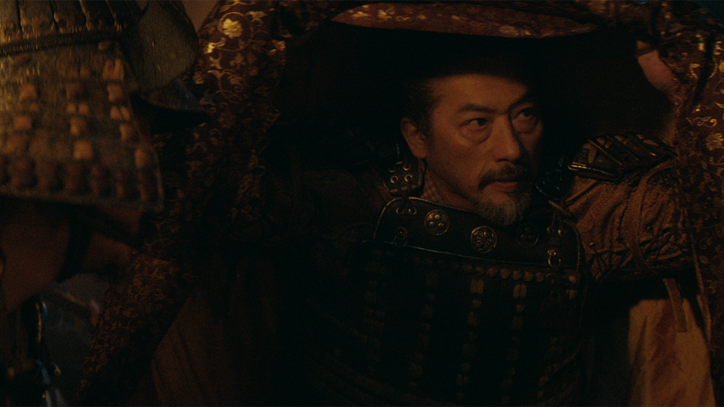 Toranaga in battle armor with a cloak covering him as he speaks to his son