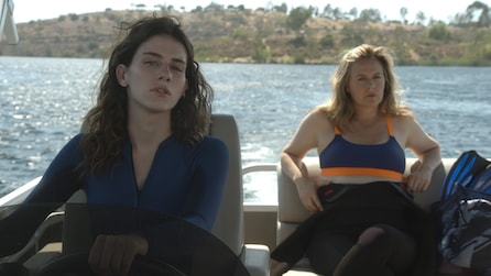 Two women on boat with one driving and the other sitting back in sports bra in American Horror Stories Installment 2