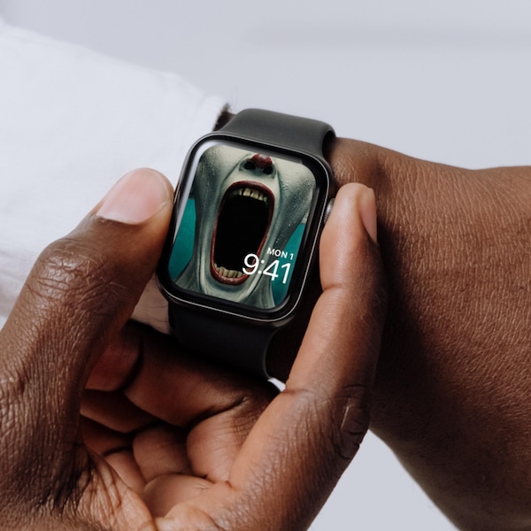 Man wearing Apple Watch with lock screen of clown in white makeup and red lipstick opening jaw wide in FX's AHS Freak Show