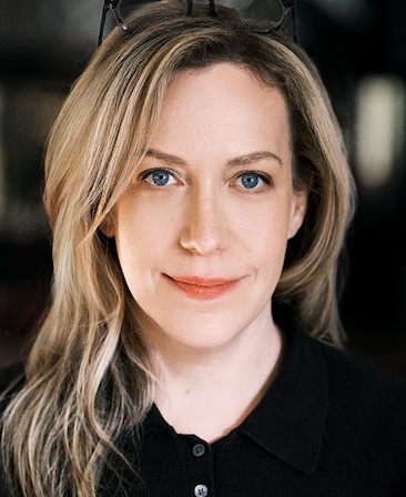 Headshot of Kim Rosenstock wearing a black button up and glasses on top of her head.