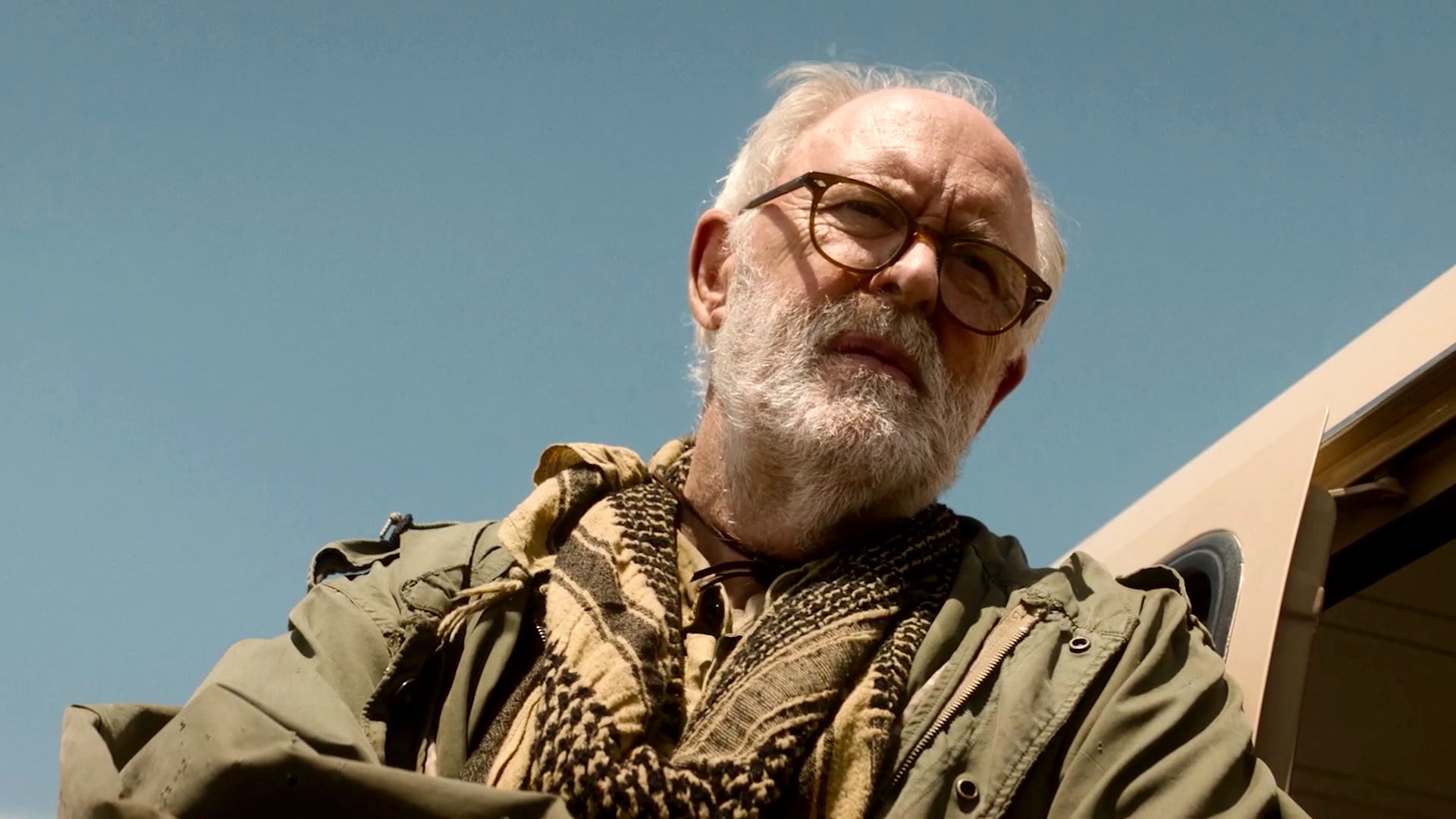 John Lithgow as Harold Harper wearing rugged green clothes, stepping out of a tan vehicle looking downwards.