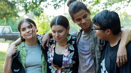 Cast of Reservation Dogs standing outside under a tree, wrapping their arms around each other