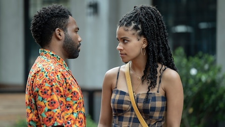 Donald Glover as Earn in bright orange graphic shirt talking to Zazie Beetz as Van in checkered dress outside in FX's Atlanta