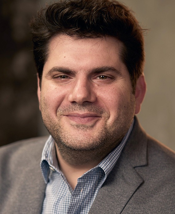 Dan Shotz headshot wearing a blue checkered button up with a grey suit