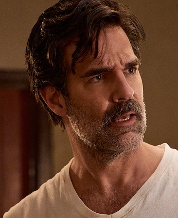 Headshot of Rob Delaney as Neighbor Guy wearing a white tshirt with a beige background.