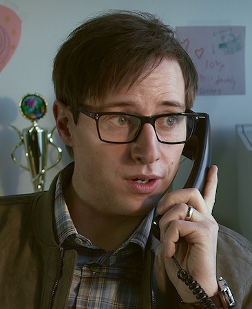 David Rysdahl headshot wearing a flannel shirt and glasses, while holding a phone to his ear