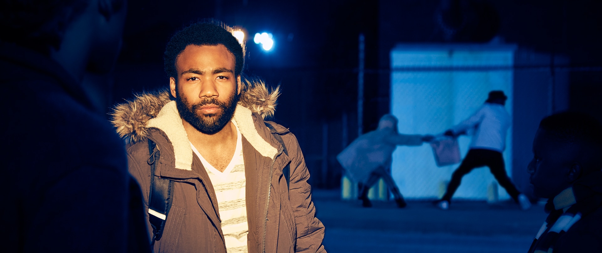 Donald Glover as Earnest Marks in a brown winter jacket with a person stealing a bag from another person behind him.
