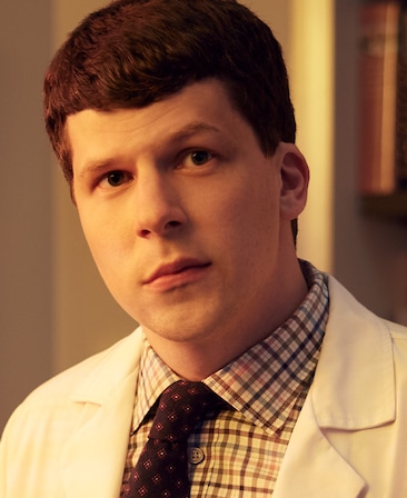 Jessie Eisenberg headshot in white doctor's coat with blue and white plaid shirt and dark colored tie, in white room