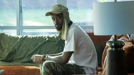LaKeith Stanfield as Darius sitting on brown couch with cargo pants and green headpiece in FX's Atlanta