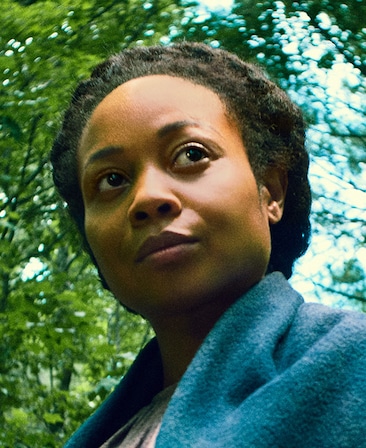 Sheria Irving headshot from lower angle in blue shawl, looking up to the side with trees and bright blue sky in background
