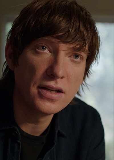 Sam leaning forward with a sliding glass window behind him