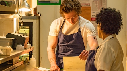 Jeremy Allen White as Carmy reading paperwork in restaurant kitchen with Liza Colón-Zayas as Tina in FX's The Bear 
