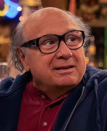 Danny DeVito headshot wearing a red polo shirt, dark blue zip up, and glasses