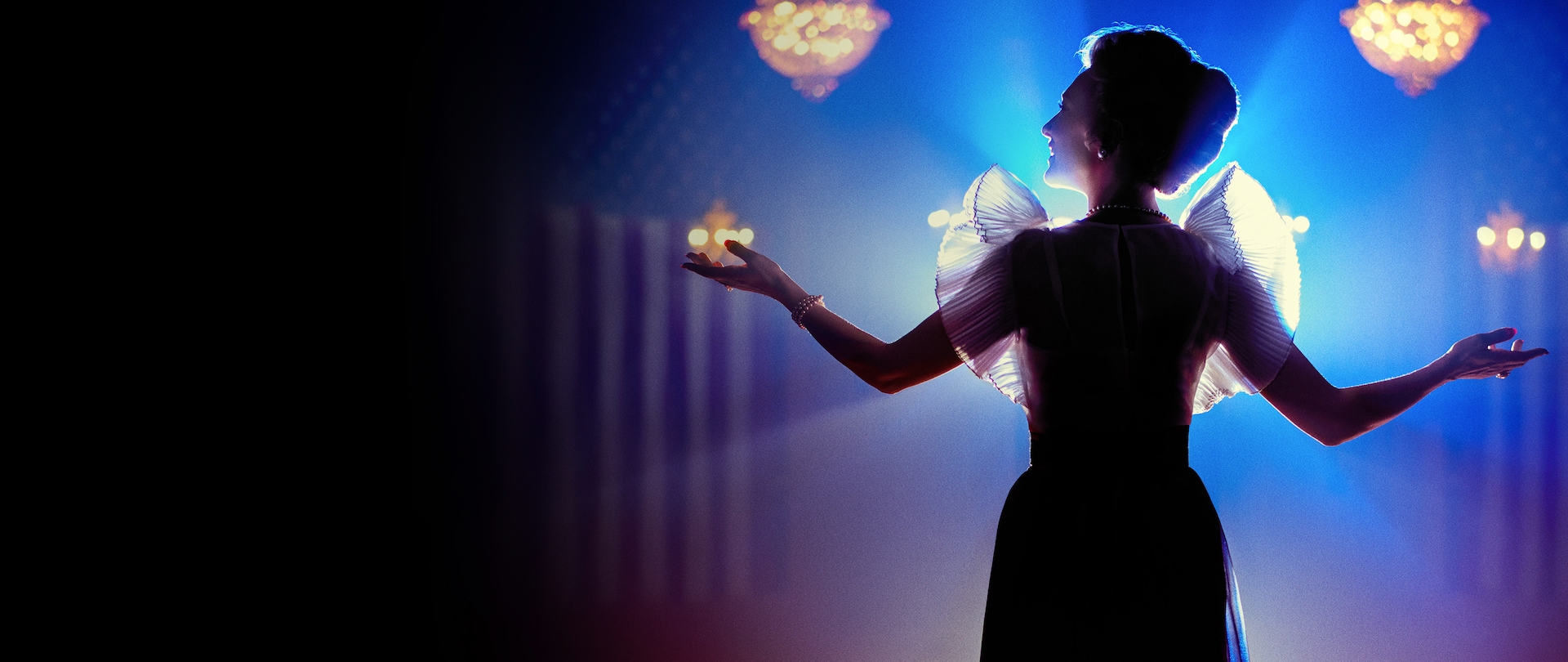 Woman holding arms out wide with blue and red lighting and chandeliers in background