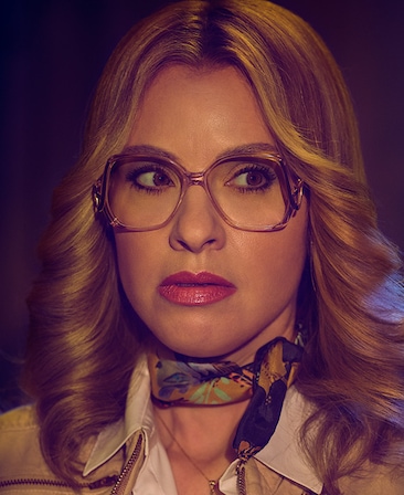 Leslie Grossman headshot with vintage glasses and swept away blonde hair and neck scarf from American Horror Story 1984