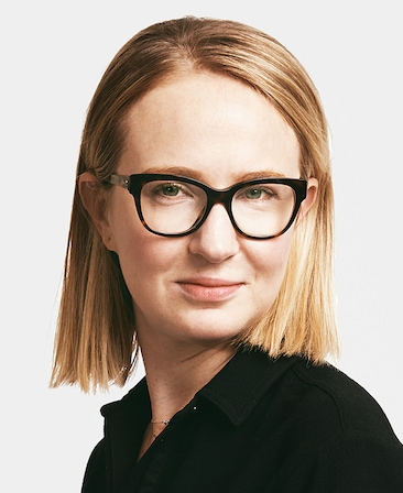 Halley Feiffer headshot wearing a black shirt and glasses standing in front of a white wall