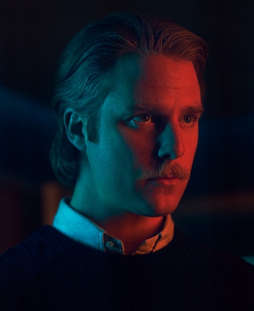 Jake McDorman wearing a sweater and collared shirt captured in red lighting for FX's Class of '09