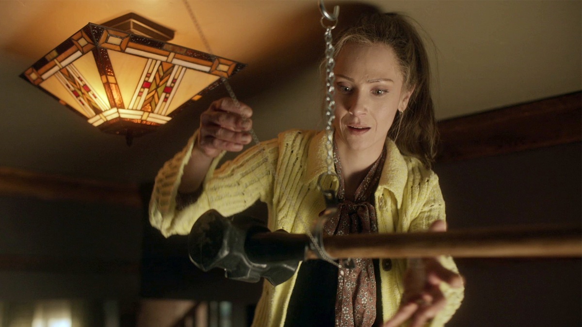 Woman wearing a yellow sweater taking a hammer to the ceiling with a chain