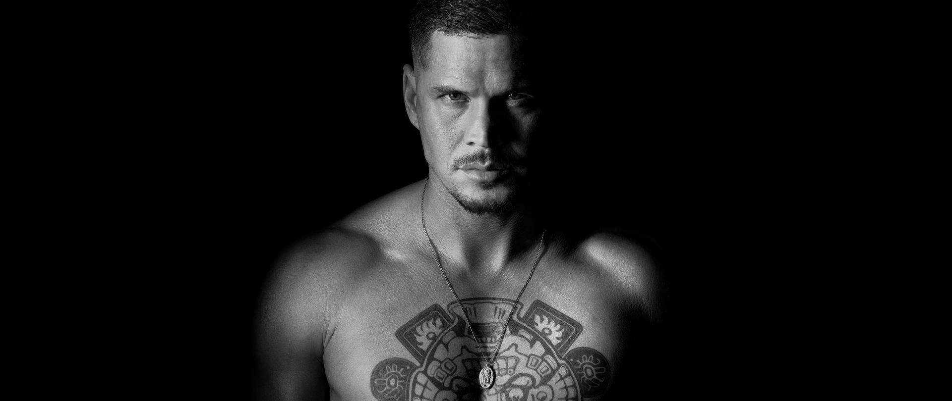JD Pardo shirtless with a chest tattoo and necklace in black and white effect