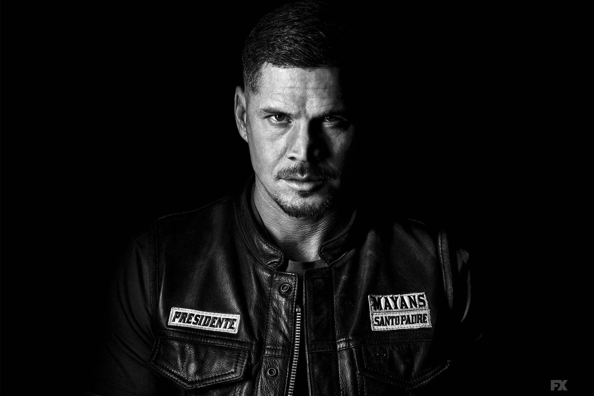 JD Pardo wearing a leather jacket with two badges that read "Presidente" and "Mayans Santo Padre"