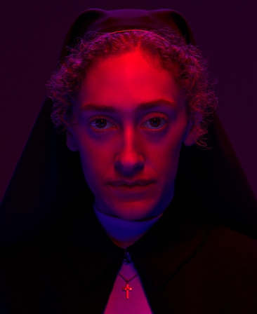 Micaela Diamond as Sister Megan Duval in FX's Grotesquerie, wearing a habit with a pink light shinning on her.