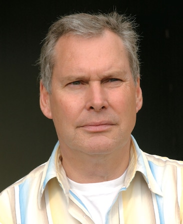 Iain Paterson headshot wearing a yellow and blue striped button up shirt over a white shirt
