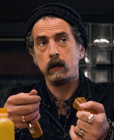 John Ales headshot holding items in his hand wearing a black beanie and silver rings
