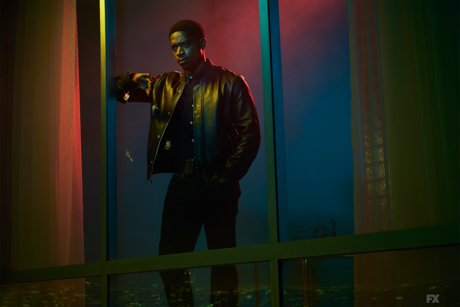 Franklin Saint wearing a leather jacket and leaning against a large window