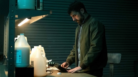 Teddy wearing a green jacket and standing by a desk in a garage