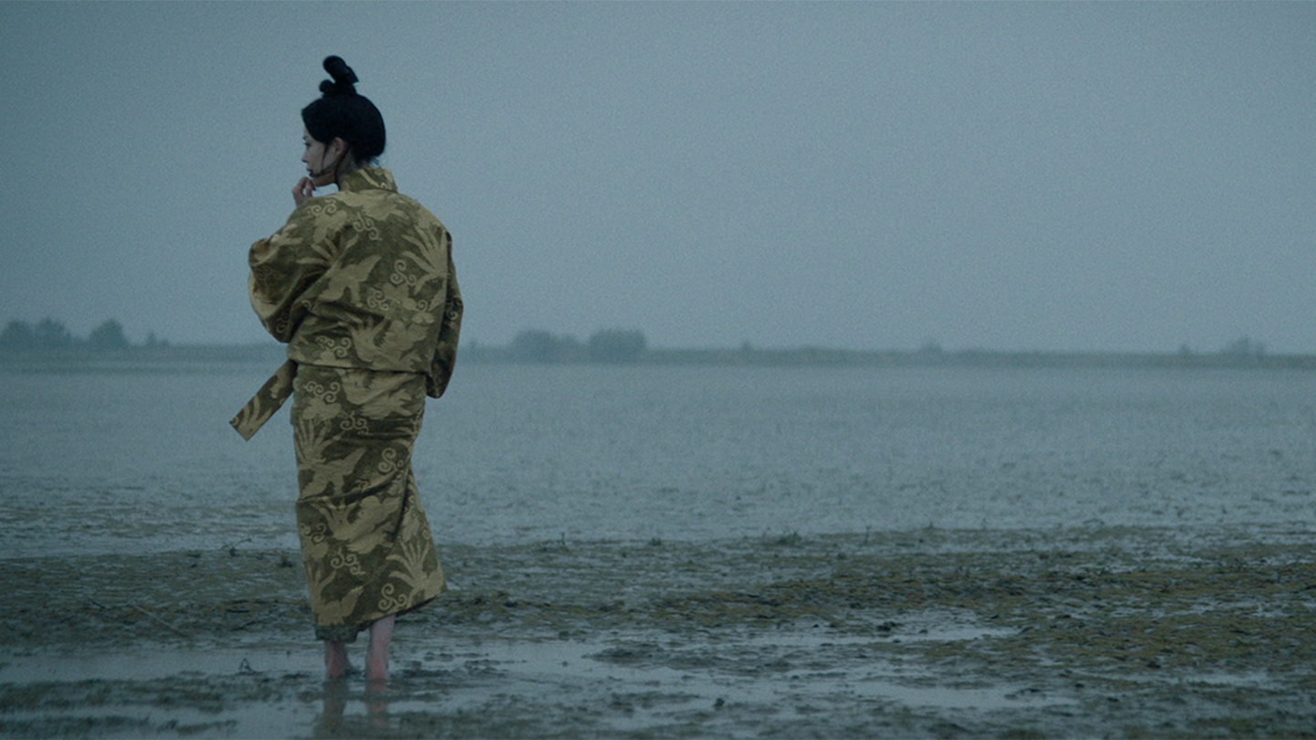 Backside of Gin dressed in yellow walking barefoot on her new Edo land