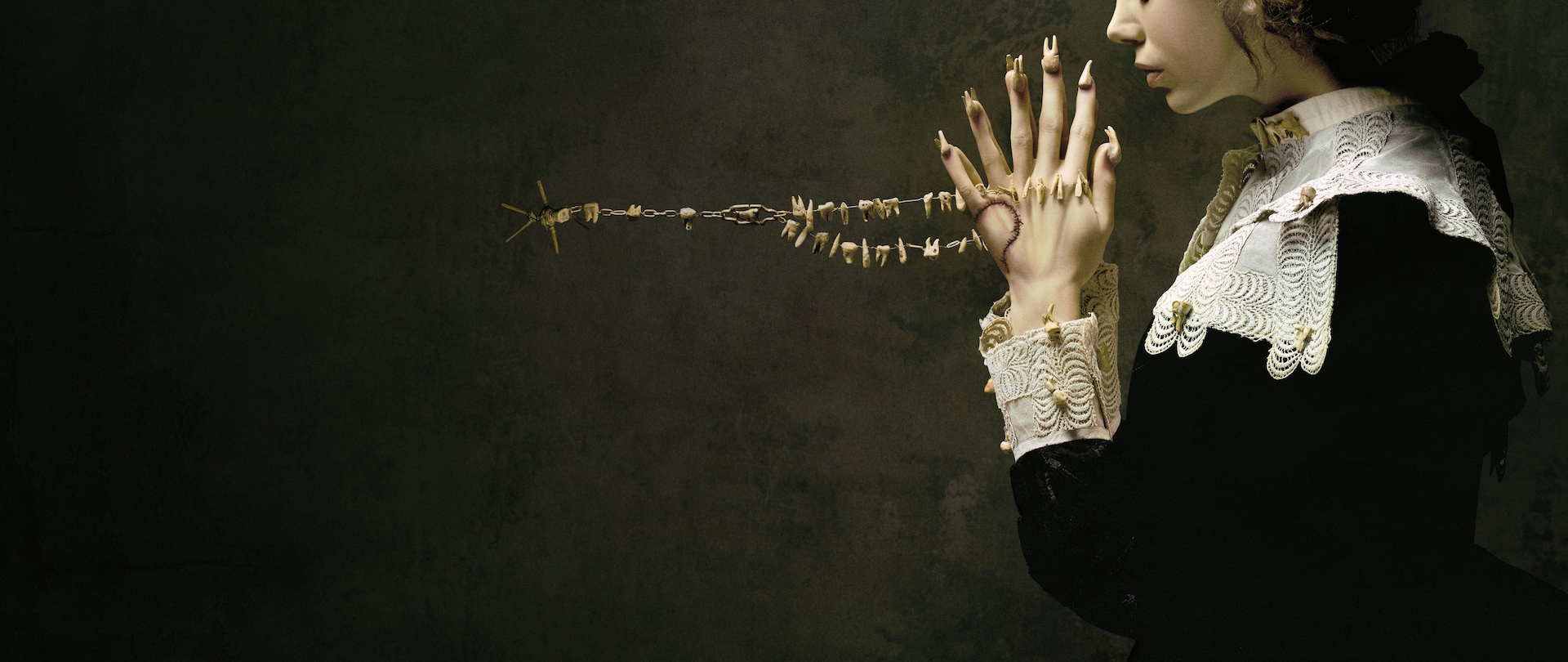 Woman in black dress with white collar and cuffs decorated with teeth, hands in prayer with nails replaced with teeth