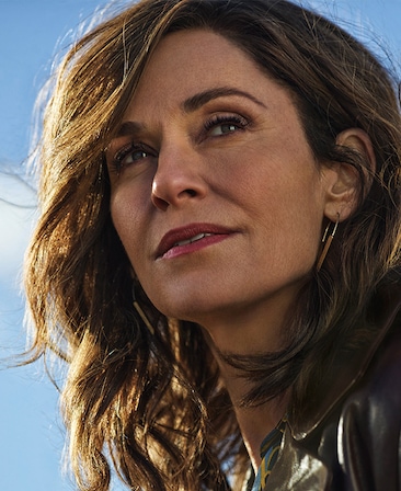 Amy Brenneman headshot wearing collar shirt with a blue sky behind her