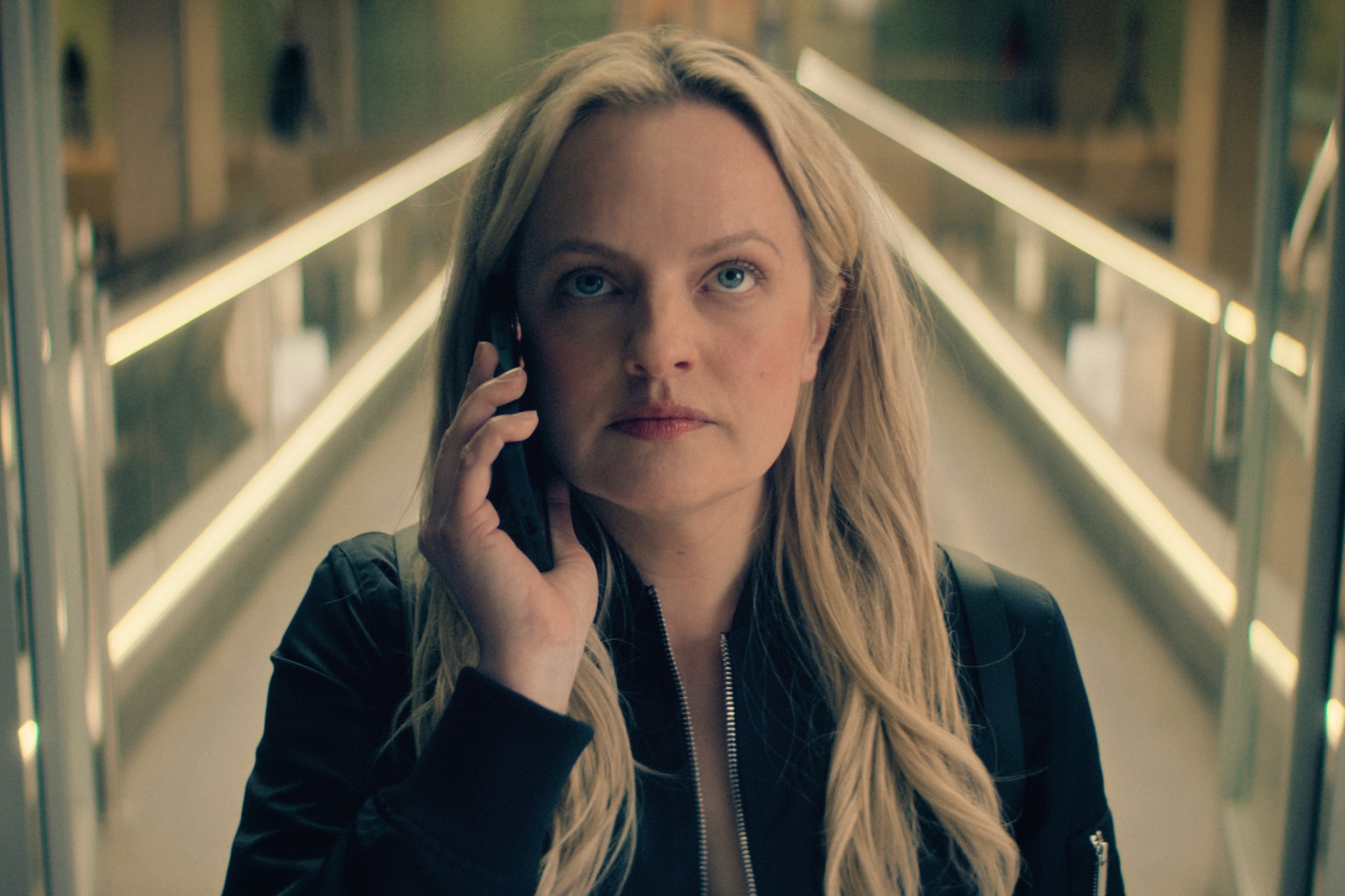 Elisabeth Moss as Imogen Salter in FX's The Veil wearing a black jacket holding a phone to her face.
