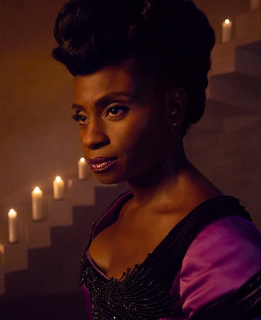 Adina Porter headshot in purple and black dress with candles on stairs from American Horror Story Apocalypse