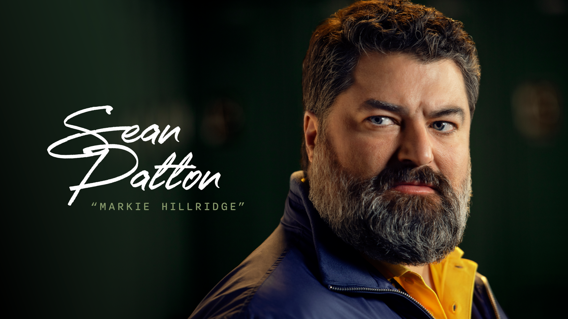 Sean Patton as Markie Hillridge in FX's English Teacher, in a green locker room, wearing a yellow and blue school jacket.