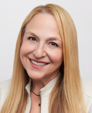 Headshot of Monica Levinson in a light leather jacket and a white background.