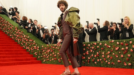 Dave Burd wearing a brown suit with puff sleeves standing on a red carpet