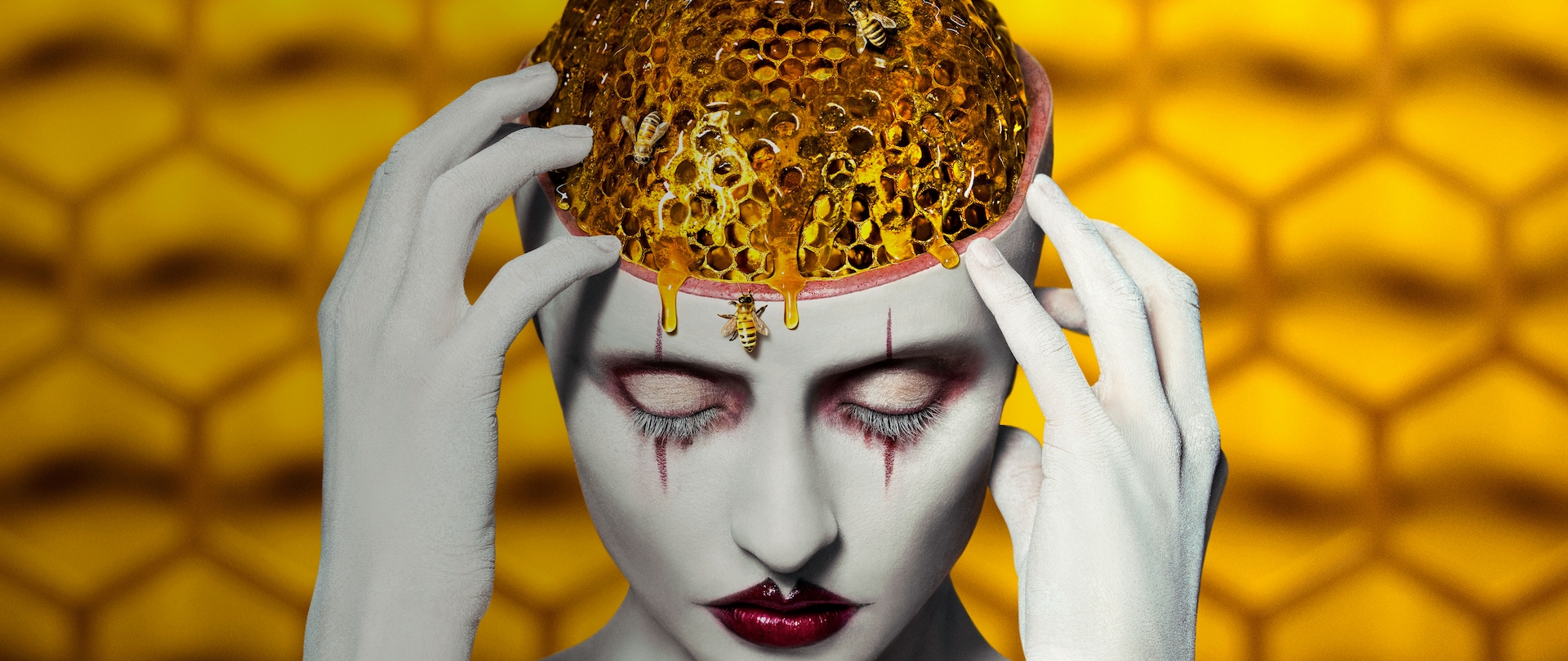 Woman in white body makeup and dark red lips touching crown of her open head that is showing a honeycomb "brain" with bees