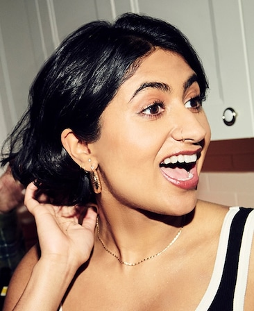 Headshot of Amita Rao as Issa in FX's Adults wearing a black and white lined tank top and gold jewelry.