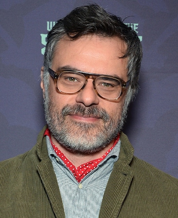 Jemaine Clement headshot wearing glasses with a green jacket.