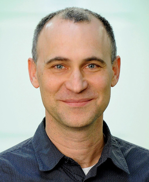 Joel Fields headshot in striped black and white button down with light blue background 