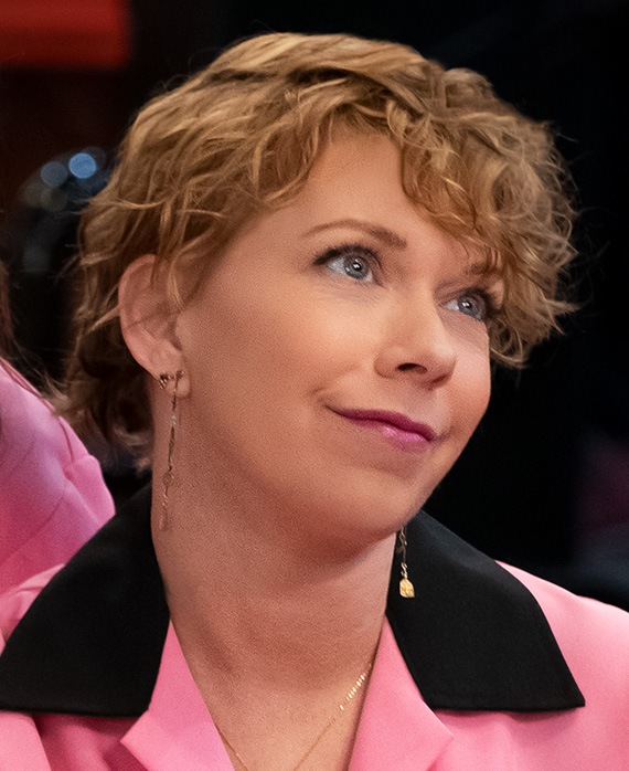 Mary Elizabeth Ellis headshot wearing a pink shirt with black collar and long earrings