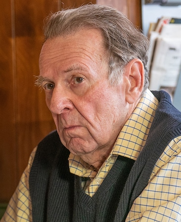 Tom Wilkinson headshot wearing a yellow plaid shirt with a gray vest over it