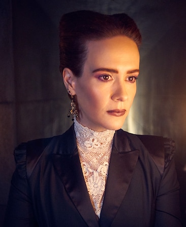 Sarah Paulson headshot in black suit dress and white lace shirt in front of shining light from AHS Apocalype